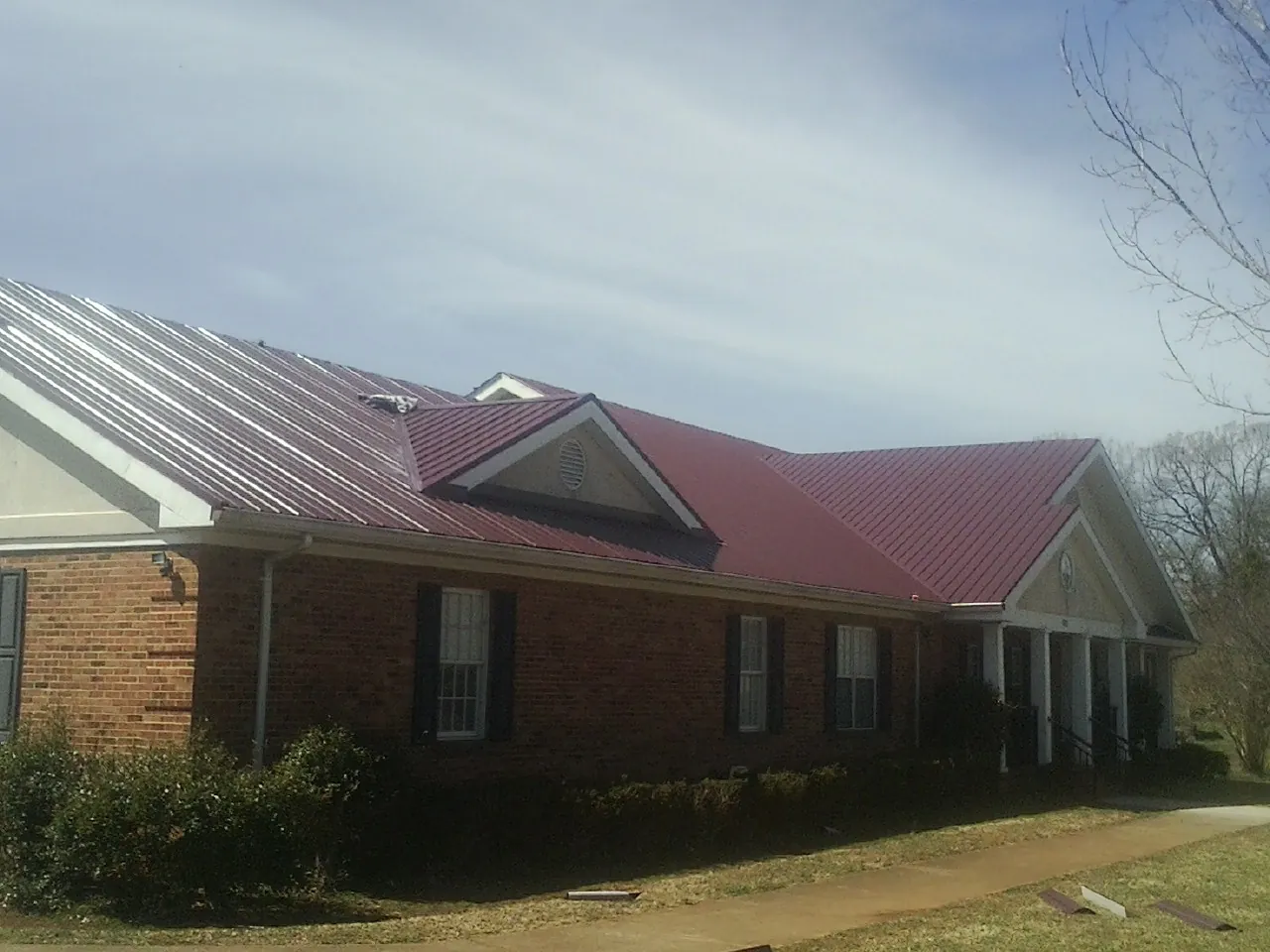 Red metal roof with gabled entries on a long brick building, from a Hail Damage Roof Repair job in Lydia