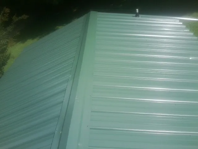 New green metal panels meeting at the ridge of a roof — Flat Roof Repair work by our crew in Lydia
