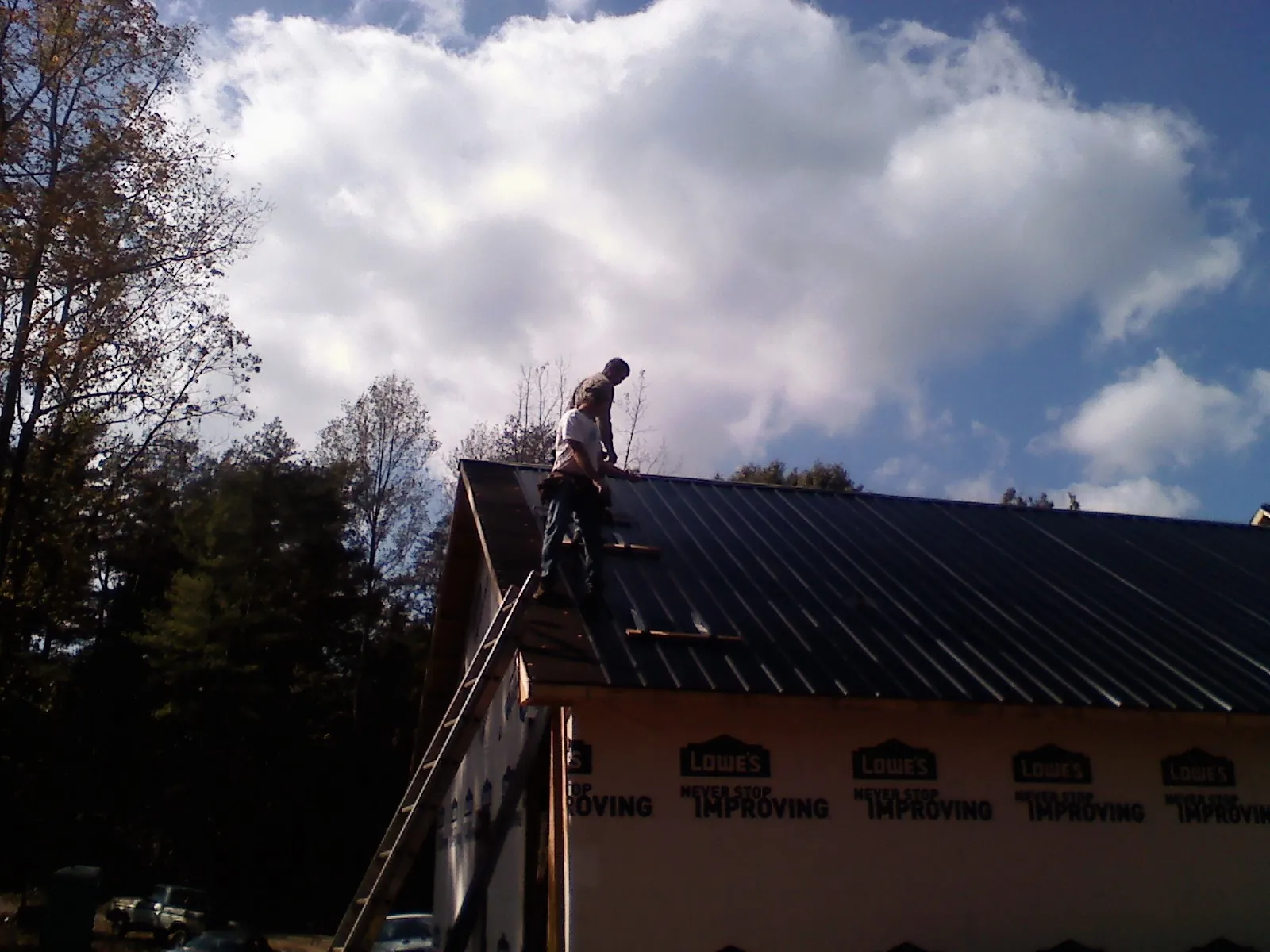 Roofer fastening dark metal panels high against a cloudy sky, from a Roof Inspection job in Lydia