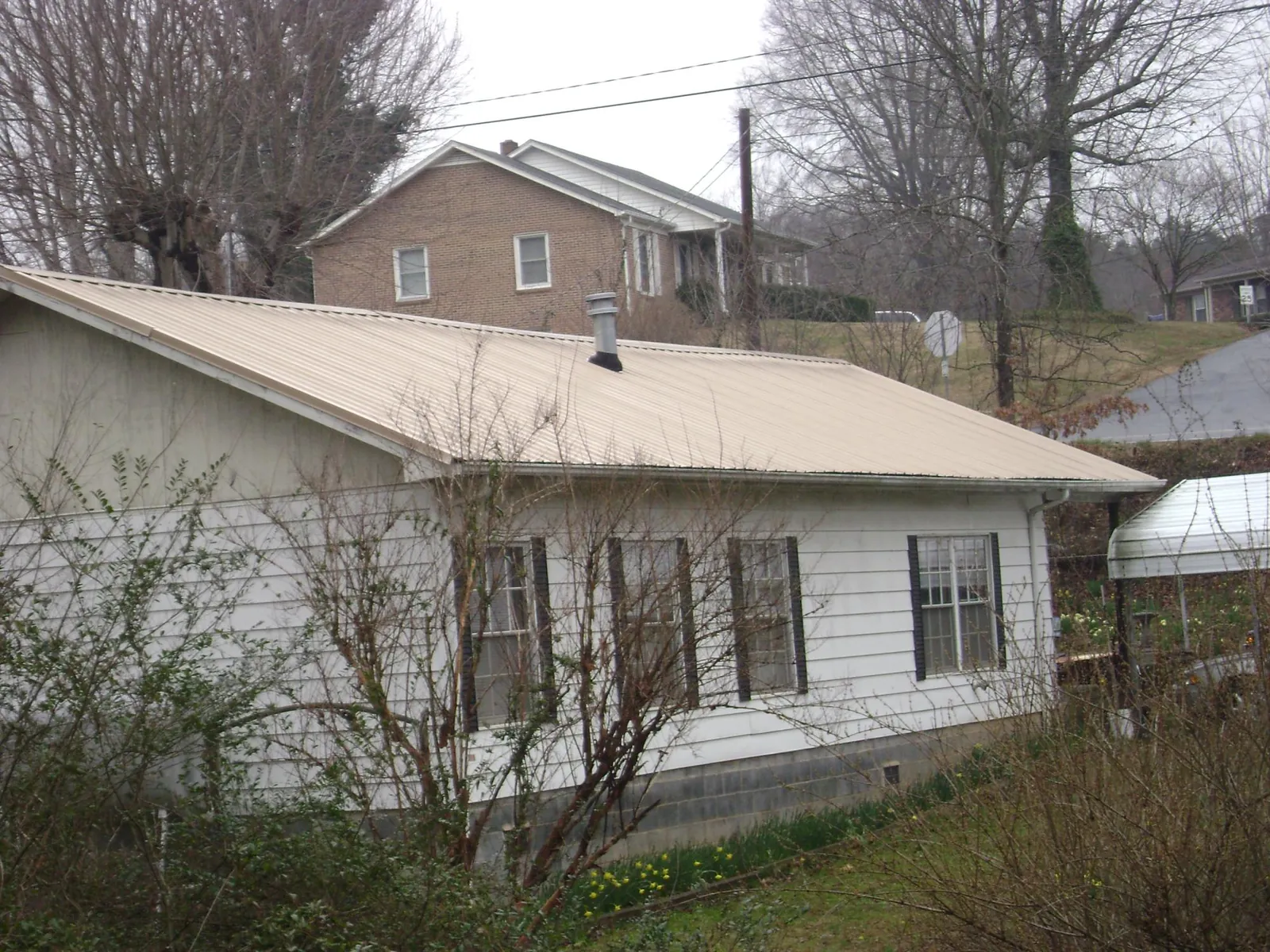Tan metal roof on a white sided house set into a hillside — Commercial Roofing by Roofing Brothers in Lydia
